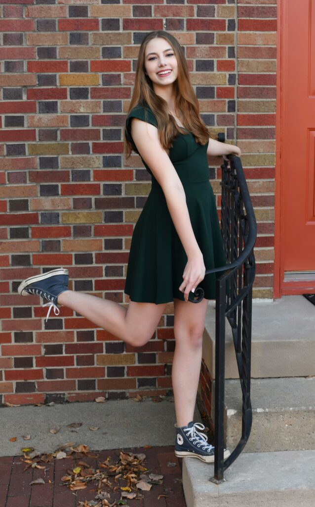 A girl in a green dress posing with her foot kicked in the air.
